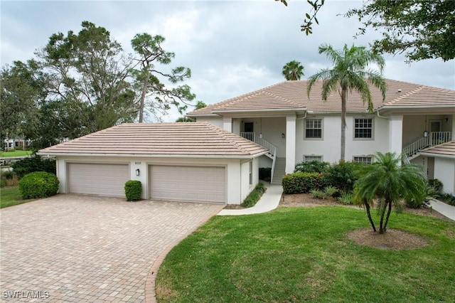 view of front of property featuring a garage, a tile roof, decorative driveway, stucco siding, and a front yard