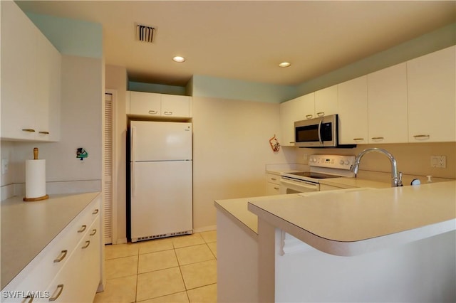 kitchen featuring light tile patterned floors, a peninsula, white appliances, visible vents, and light countertops