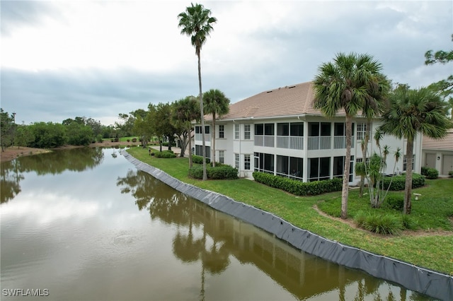 back of property with a water view, a sunroom, and a lawn