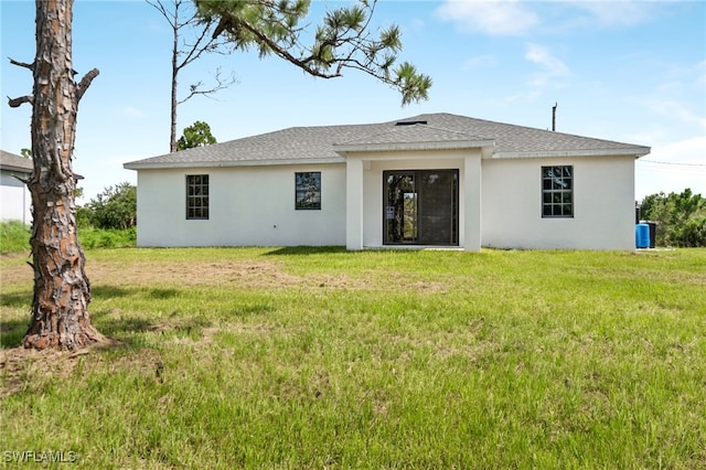 rear view of house with a shingled roof, a lawn, and stucco siding