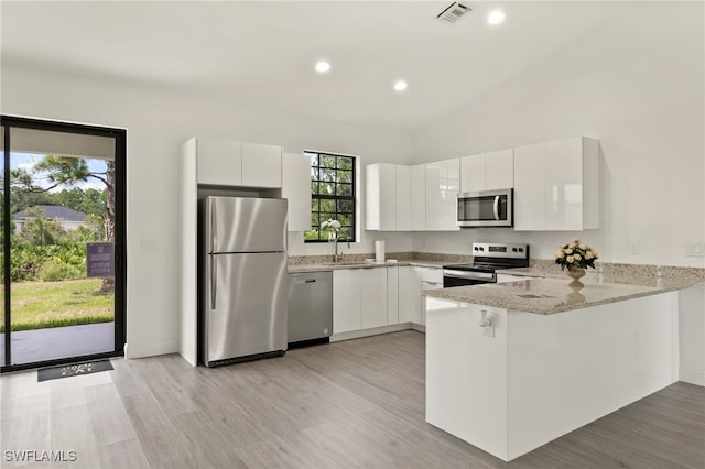 kitchen featuring light wood-type flooring, appliances with stainless steel finishes, light stone countertops, white cabinetry, and kitchen peninsula