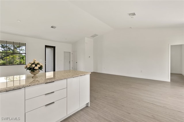 kitchen featuring light hardwood / wood-style floors, white cabinets, light stone countertops, and lofted ceiling