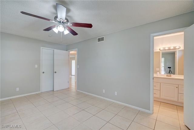 unfurnished bedroom with connected bathroom, ceiling fan, light tile patterned floors, and a textured ceiling