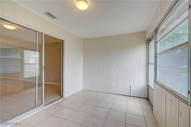 unfurnished room with a textured ceiling, wood walls, and light tile patterned floors