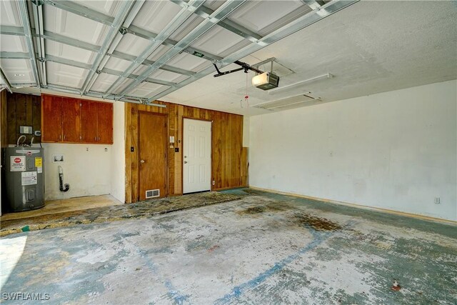 garage featuring a garage door opener, wood walls, and electric water heater