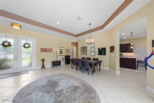 dining area featuring a raised ceiling, an inviting chandelier, french doors, and light tile patterned flooring