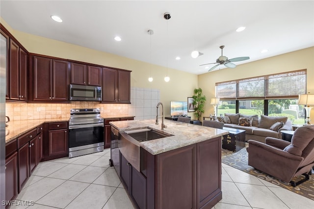 kitchen with a kitchen island with sink, stainless steel appliances, sink, ceiling fan, and light stone countertops