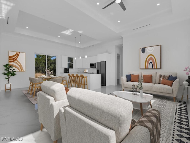 living room with a raised ceiling, ceiling fan, sink, and a high ceiling
