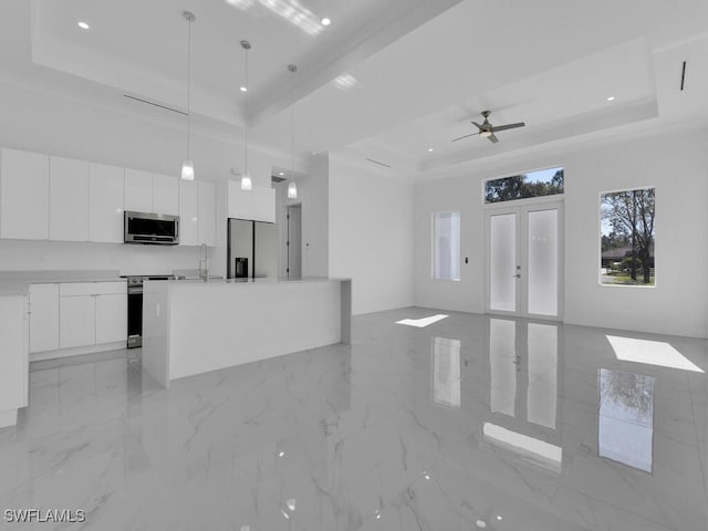 kitchen with a raised ceiling, white cabinetry, stainless steel appliances, and decorative light fixtures