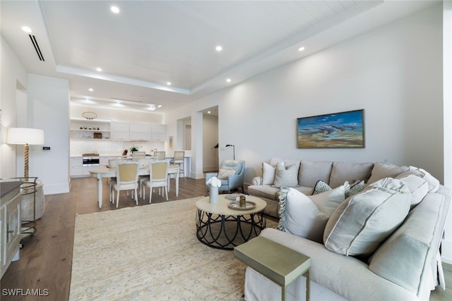 living area with light wood-type flooring, a raised ceiling, baseboards, and recessed lighting