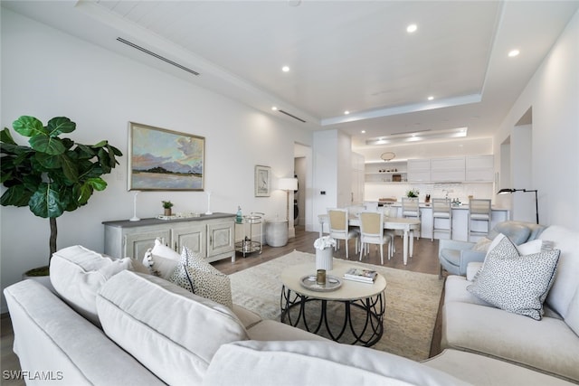 living area with baseboards, wood finished floors, a raised ceiling, and recessed lighting