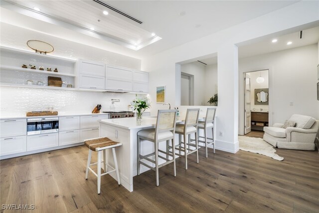 kitchen featuring white cabinetry, a center island, a kitchen breakfast bar, tasteful backsplash, and hardwood / wood-style floors