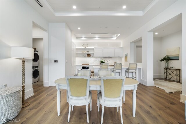 dining area with a tray ceiling, crown molding, dark hardwood / wood-style flooring, and stacked washing maching and dryer