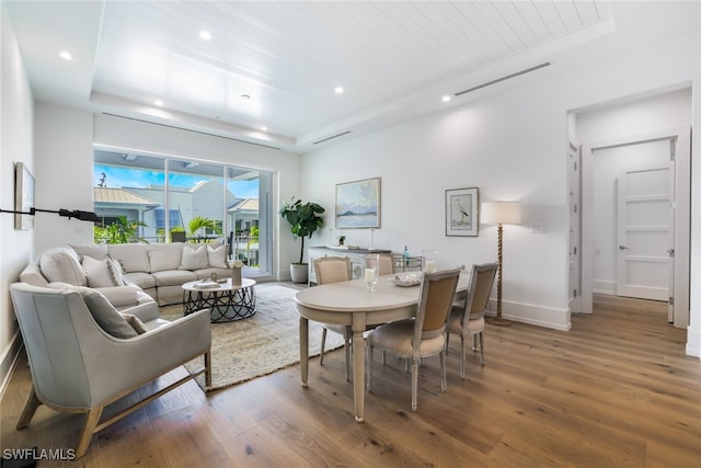 dining area with a tray ceiling, visible vents, baseboards, and wood finished floors