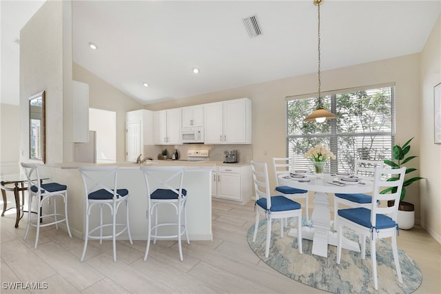 kitchen featuring decorative light fixtures, white cabinetry, sink, kitchen peninsula, and vaulted ceiling