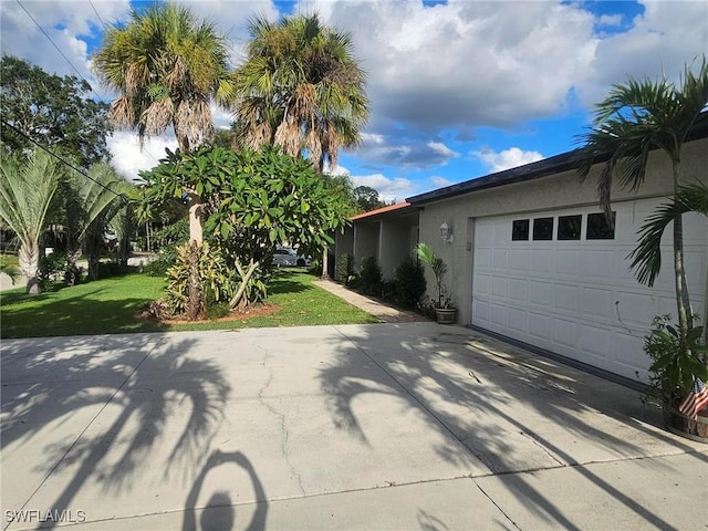 exterior space with an attached garage, concrete driveway, a front yard, and stucco siding