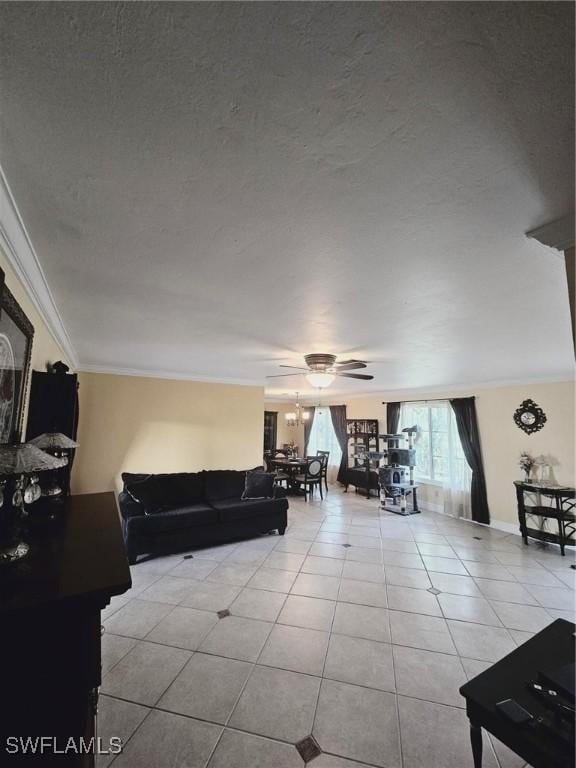 living area with light tile patterned floors, a textured ceiling, a ceiling fan, baseboards, and ornamental molding