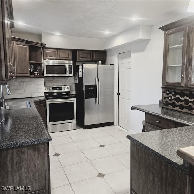 kitchen featuring dark brown cabinetry, tasteful backsplash, dark countertops, appliances with stainless steel finishes, and a sink