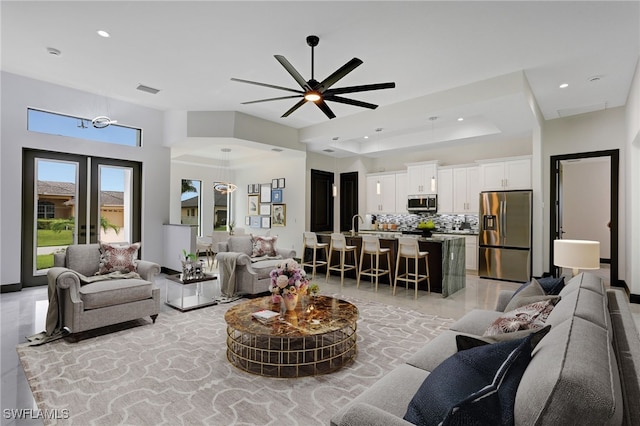 living room with ceiling fan with notable chandelier, a raised ceiling, and french doors