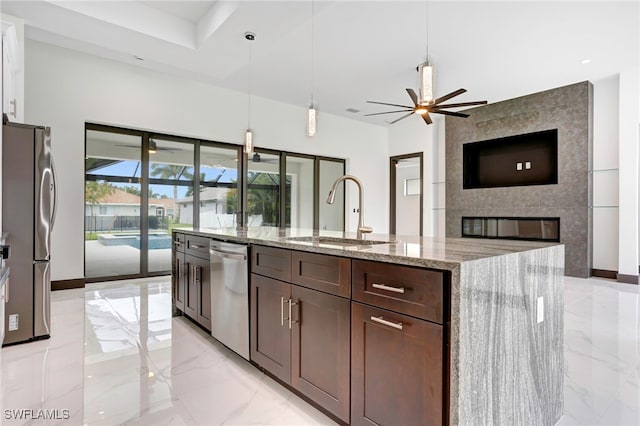 kitchen featuring sink, light stone counters, a center island with sink, stainless steel appliances, and a tiled fireplace