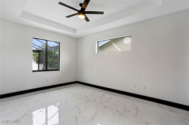 unfurnished room featuring ceiling fan, a raised ceiling, and a healthy amount of sunlight