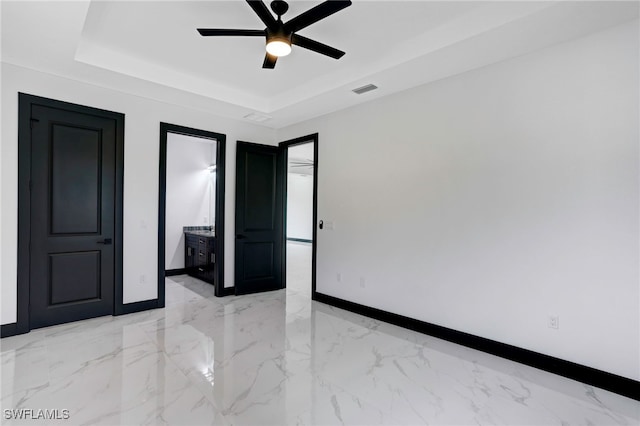 unfurnished bedroom with a tray ceiling, ensuite bath, and ceiling fan