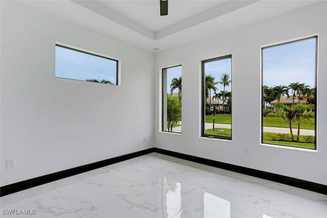 spare room featuring a ceiling fan, a tray ceiling, marble finish floor, and baseboards