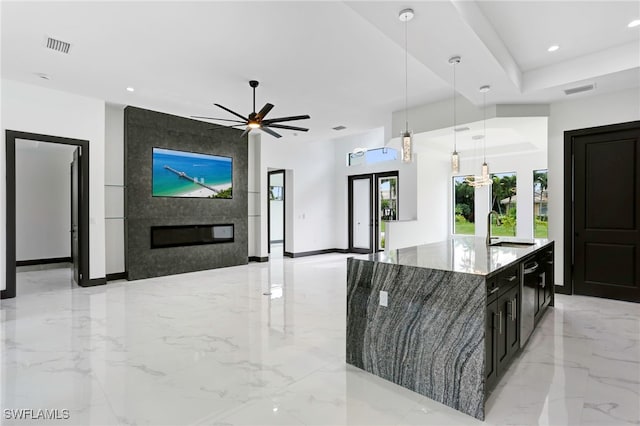 kitchen featuring pendant lighting, sink, ceiling fan, a kitchen island with sink, and light stone counters