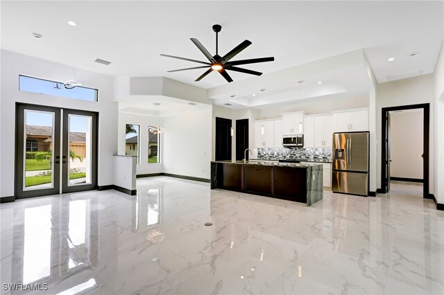 kitchen featuring appliances with stainless steel finishes, a kitchen island with sink, white cabinetry, decorative backsplash, and ceiling fan with notable chandelier