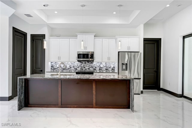 kitchen featuring white cabinetry, light stone counters, a tray ceiling, stainless steel appliances, and a kitchen island with sink