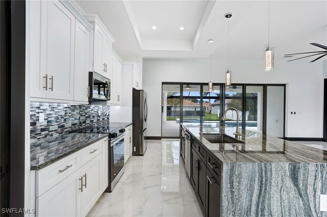 kitchen featuring sink, dark stone countertops, pendant lighting, stainless steel appliances, and white cabinets