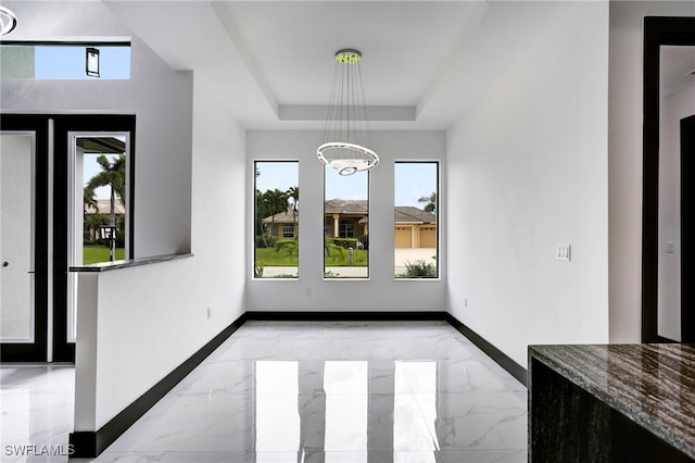 unfurnished dining area featuring a raised ceiling, marble finish floor, and baseboards