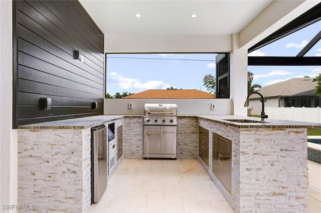 view of patio with glass enclosure, an outdoor kitchen, a sink, and fence