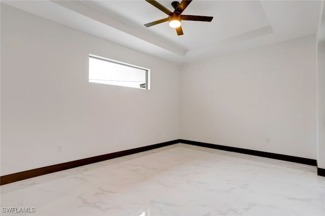 empty room featuring ceiling fan and a tray ceiling