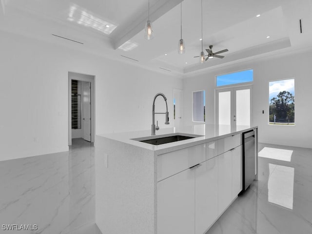 kitchen with a tray ceiling, a kitchen island with sink, sink, decorative light fixtures, and white cabinetry