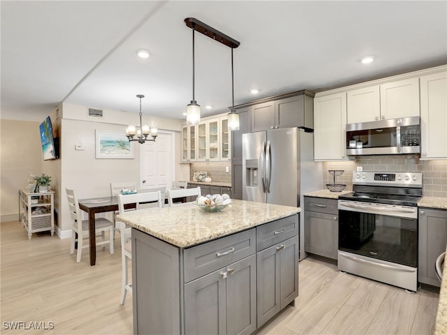 kitchen featuring appliances with stainless steel finishes, hanging light fixtures, decorative backsplash, and gray cabinetry