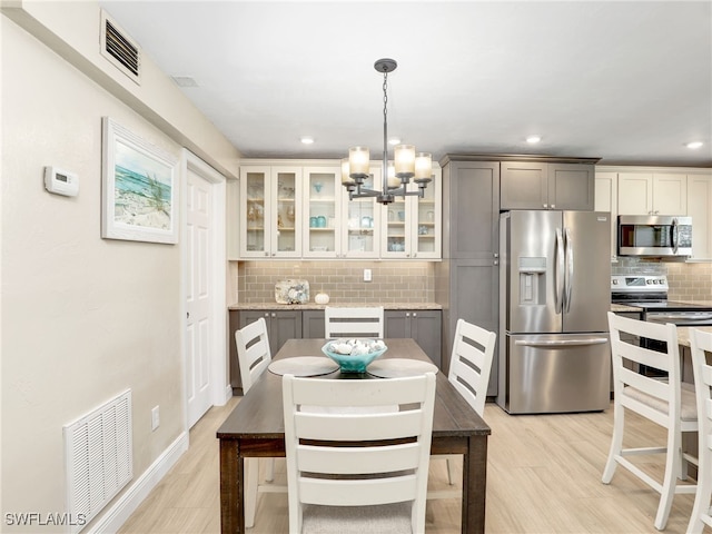 kitchen featuring decorative light fixtures, gray cabinets, stainless steel appliances, light wood-type flooring, and decorative backsplash