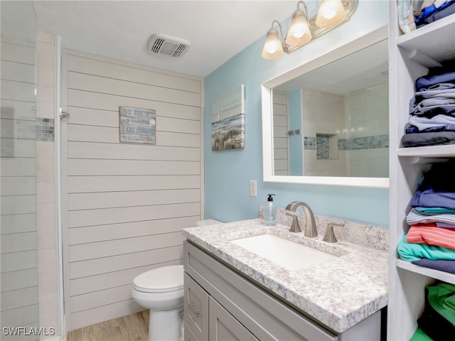 bathroom featuring vanity, wood-type flooring, a tile shower, wooden walls, and toilet