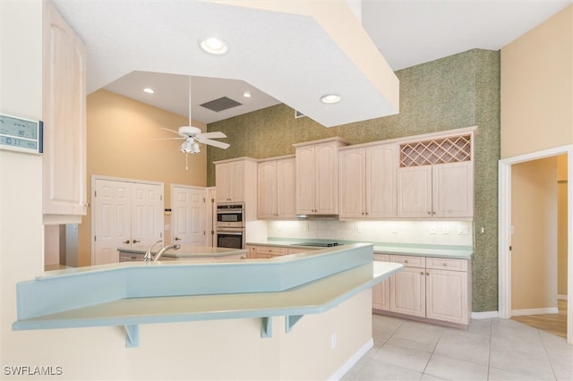 kitchen with a kitchen bar, a high ceiling, stainless steel double oven, decorative backsplash, and ceiling fan