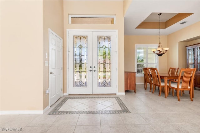 foyer entrance with a raised ceiling, light tile patterned flooring, a healthy amount of sunlight, and french doors