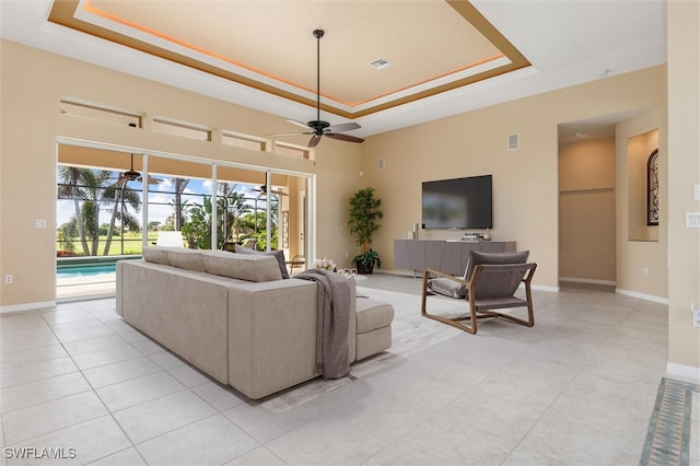 living room with light tile patterned flooring, ceiling fan, and a raised ceiling