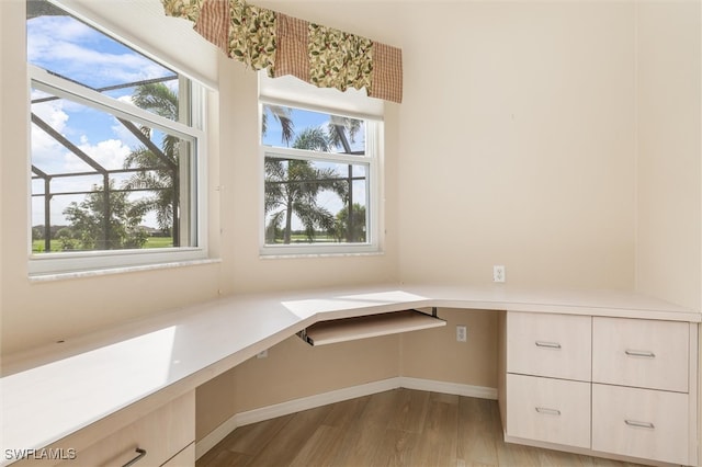 unfurnished office featuring light hardwood / wood-style flooring, a healthy amount of sunlight, and built in desk