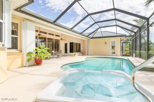 view of swimming pool with glass enclosure, ceiling fan, an in ground hot tub, and a patio