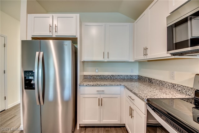 kitchen with stainless steel appliances, white cabinetry, light stone countertops, lofted ceiling, and wood-type flooring