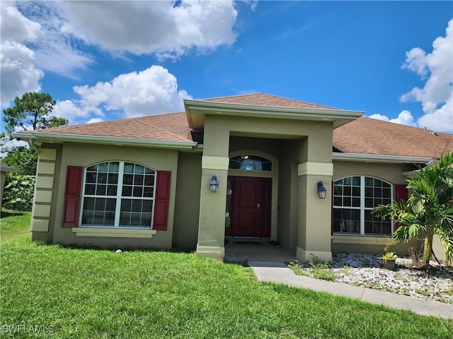 915 Alvin Ave, Lehigh Acres, FL 33971 - view of front of house with stucco siding, a front yard, and roof with shingles