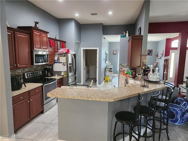 kitchen featuring light tile patterned flooring, backsplash, a breakfast bar, appliances with stainless steel finishes, and kitchen peninsula