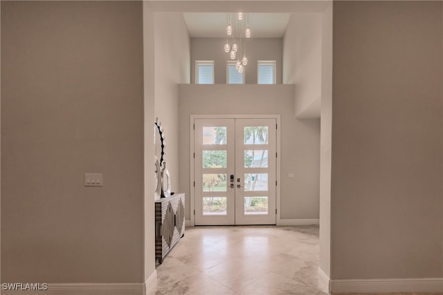 tiled foyer featuring french doors, a high ceiling, and a notable chandelier