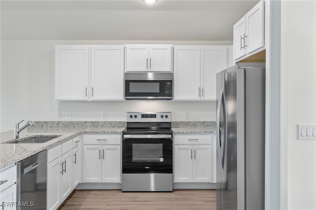 kitchen with white cabinets, light wood-type flooring, light stone countertops, and stainless steel appliances