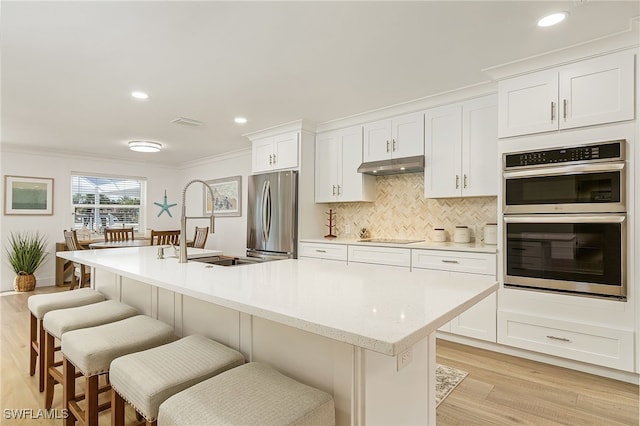 kitchen with a kitchen island with sink, light wood-type flooring, appliances with stainless steel finishes, and ornamental molding