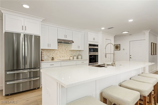 kitchen with stainless steel appliances, backsplash, white cabinets, and under cabinet range hood